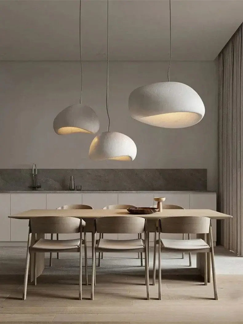 Modern pendant lights in a minimalist dining room, illuminating a light wood table and chairs with a neutral backdrop.