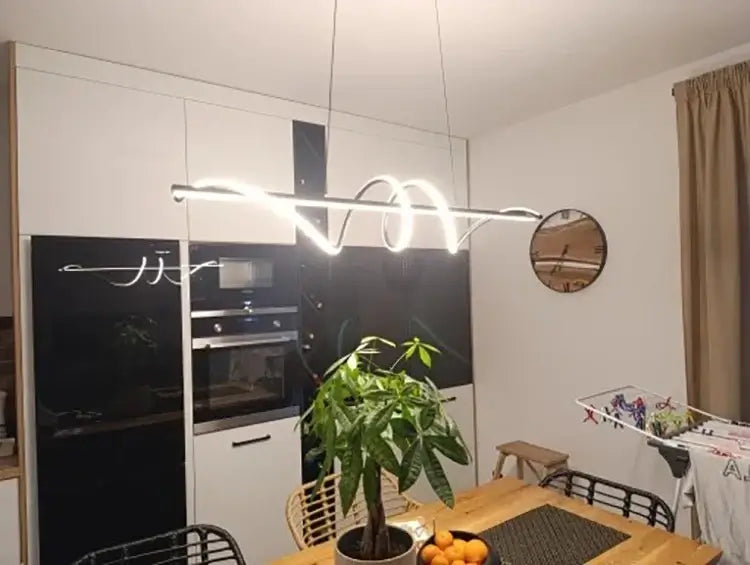 Modern LED pendant light hanging above a dining table with greenery, enhancing a minimalist kitchen decor.